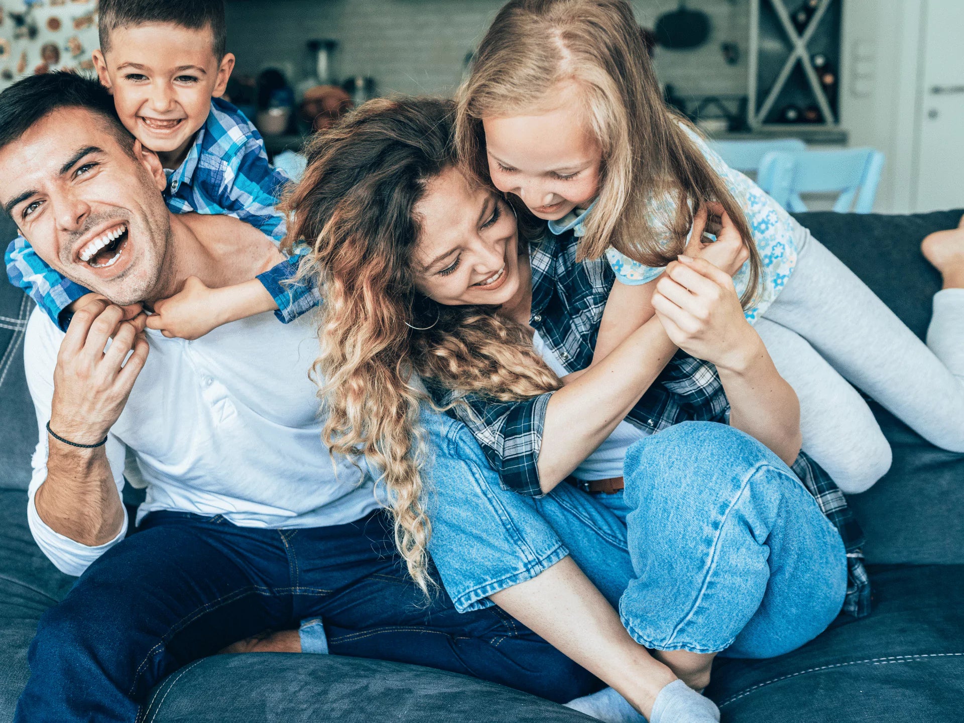 Father, son, mother, and daughter laughing and hugging on couch